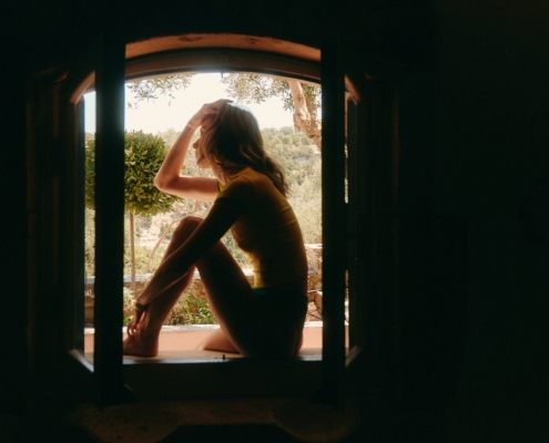 vrouw zit bij raam en denkt na over relatie met emotioneel onbeschikbare partner