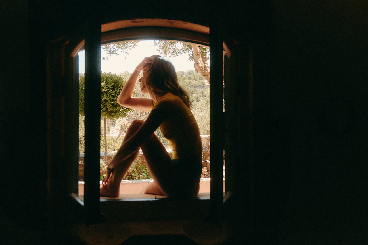 emotionele-afstand-relatie vrouw zit bij raam en denkt na over relatie met emotioneel onbeschikbare partner